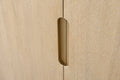 Close-up of recessed brass cabinet pull handle on light oak wood vanity door