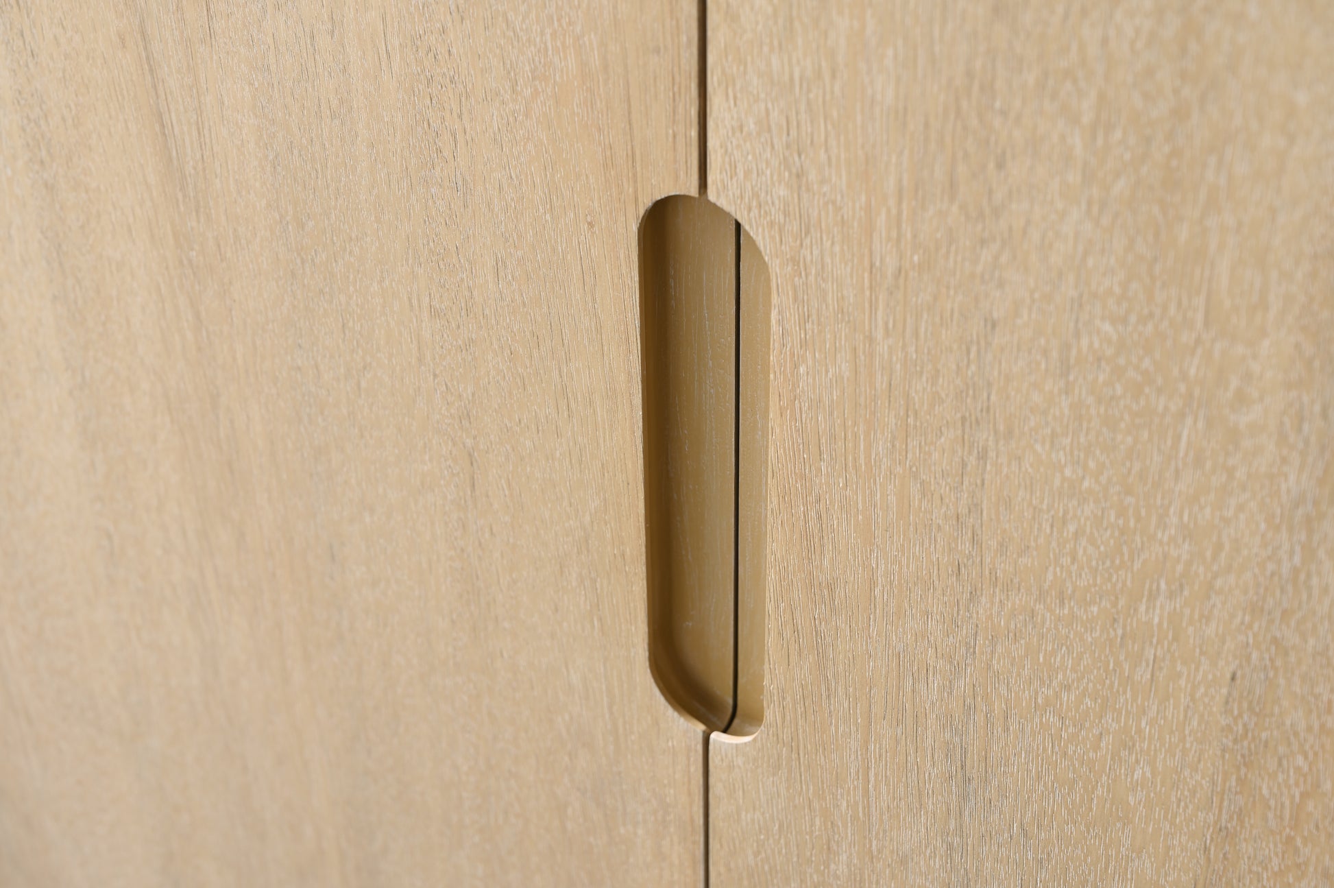 Close-up of recessed brass cabinet pull handle on light oak wood vanity door