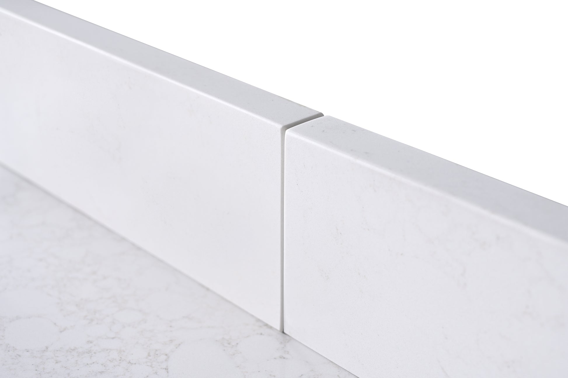 Close-up edge profile of white engineered stone backsplash and countertop with subtle marble veining