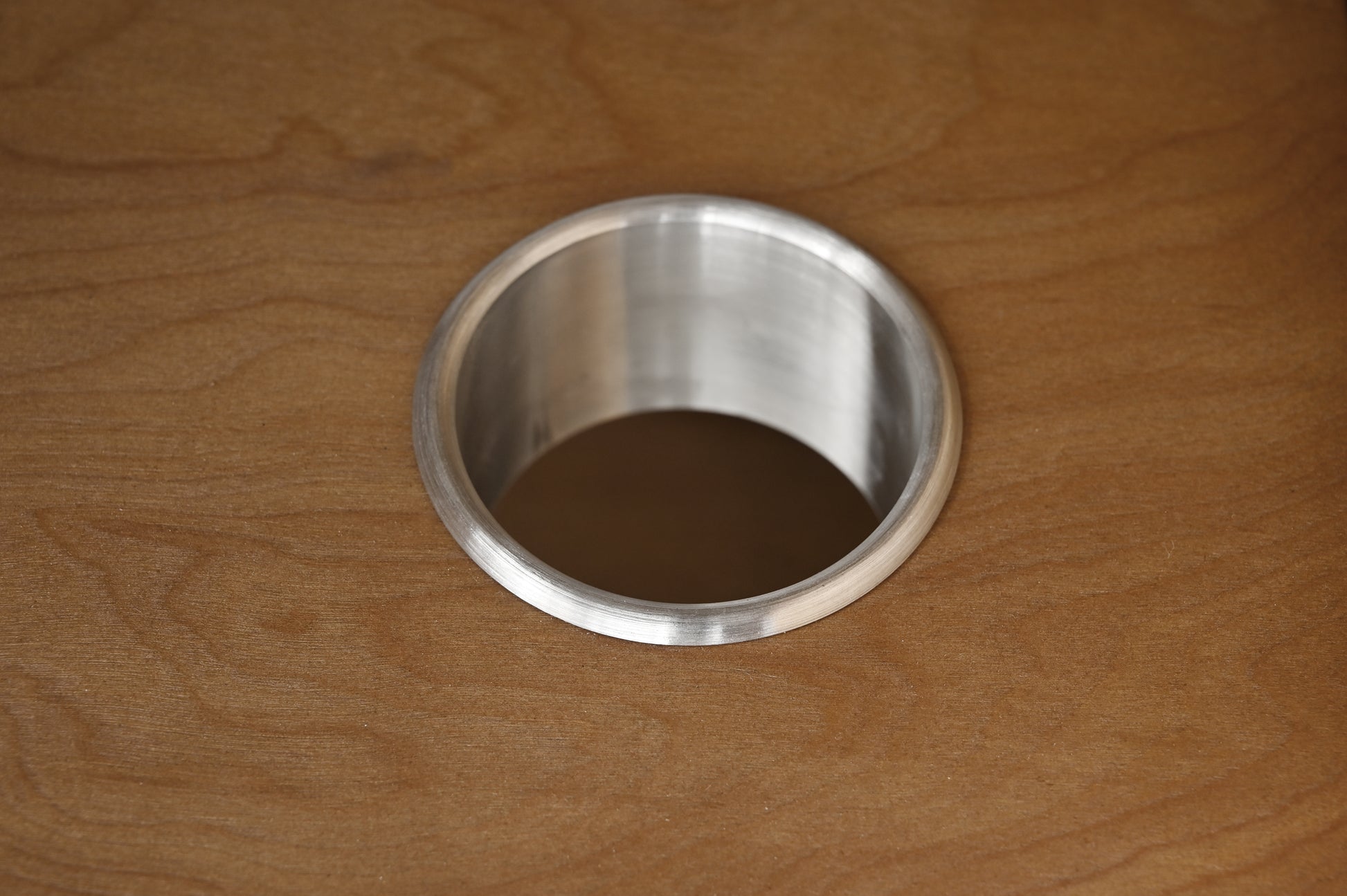 Detail of round brushed stainless steel cable management grommet on walnut vanity pull-out tray