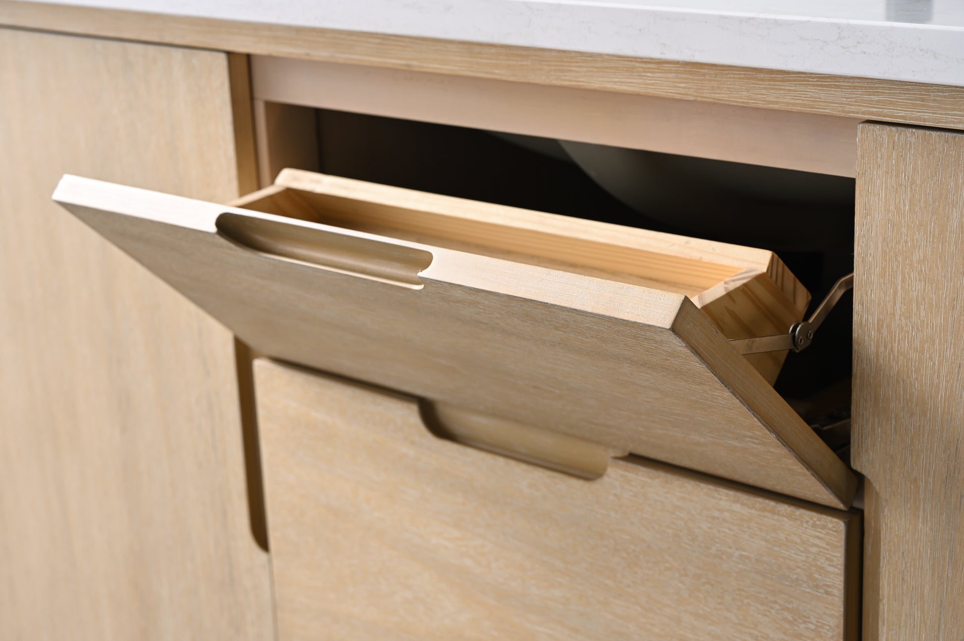 Close-up of tilt-out vanity drawer open revealing angled wooden interior tray with finger-pull handle