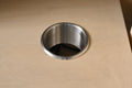 Top-down close-up of stainless steel cable management grommet on pull-out power shelf inside bathroom vanity