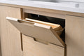Close-up of top tilt-out drawer open on light oak vanity cabinet showing hidden storage compartment