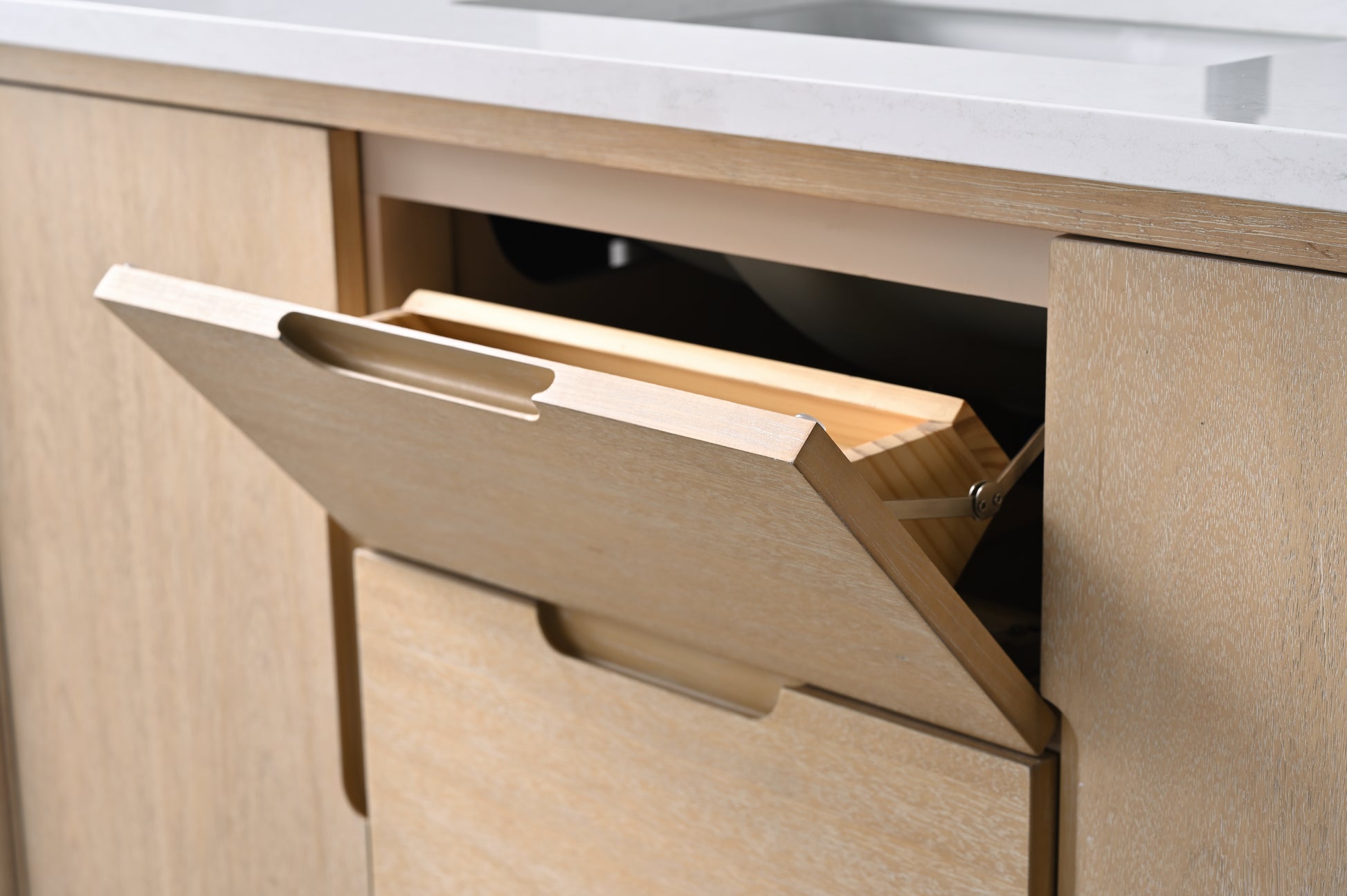 Close-up of top tilt-out drawer open on light oak vanity cabinet showing hidden storage compartment