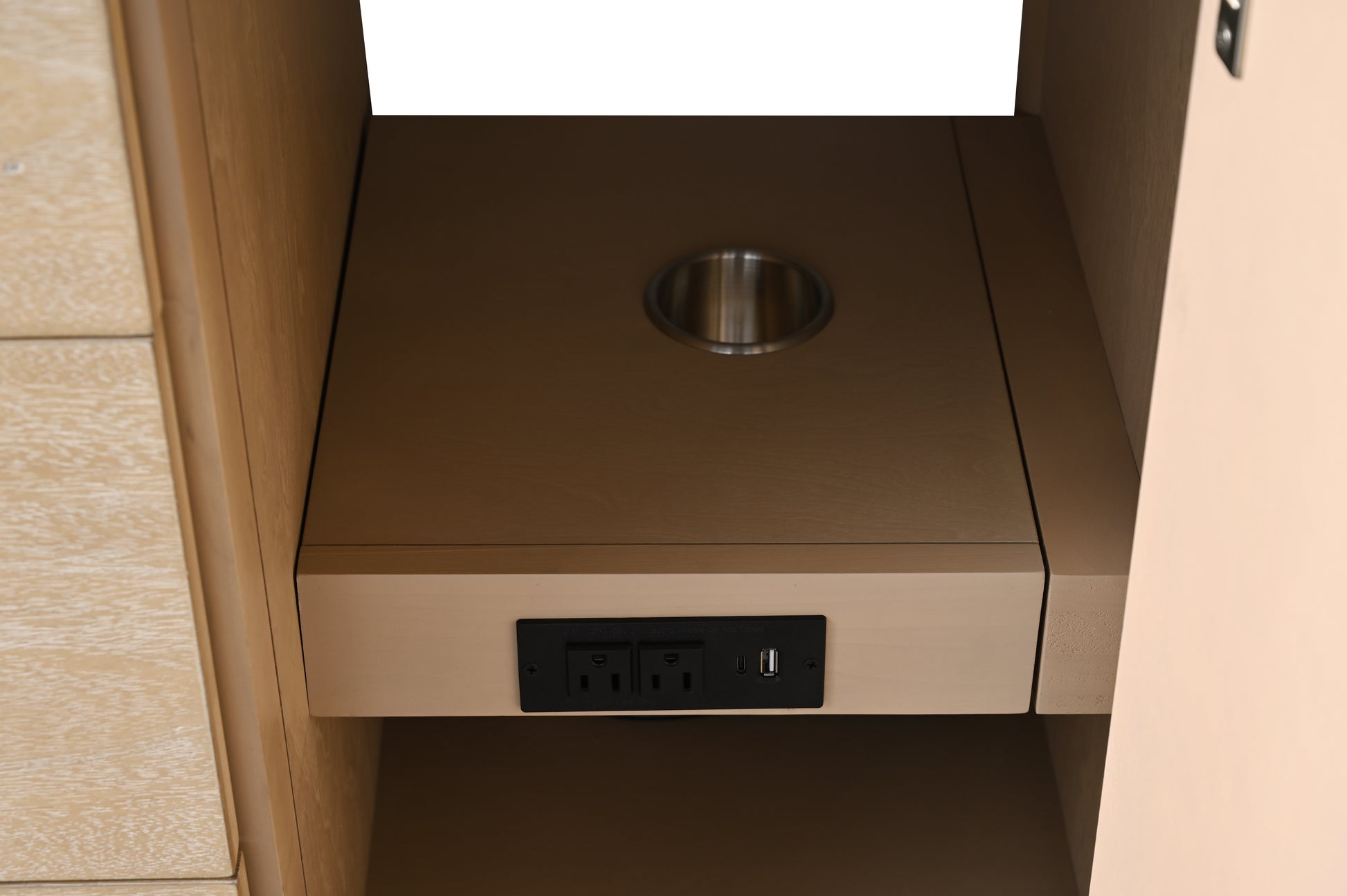 Interior view of vanity cabinet showing pull-out shelf with electrical outlets, USB port, and round cutout