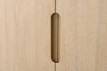 Close-up of recessed elongated brass pull handle centered on light oak double-door vanity cabinet