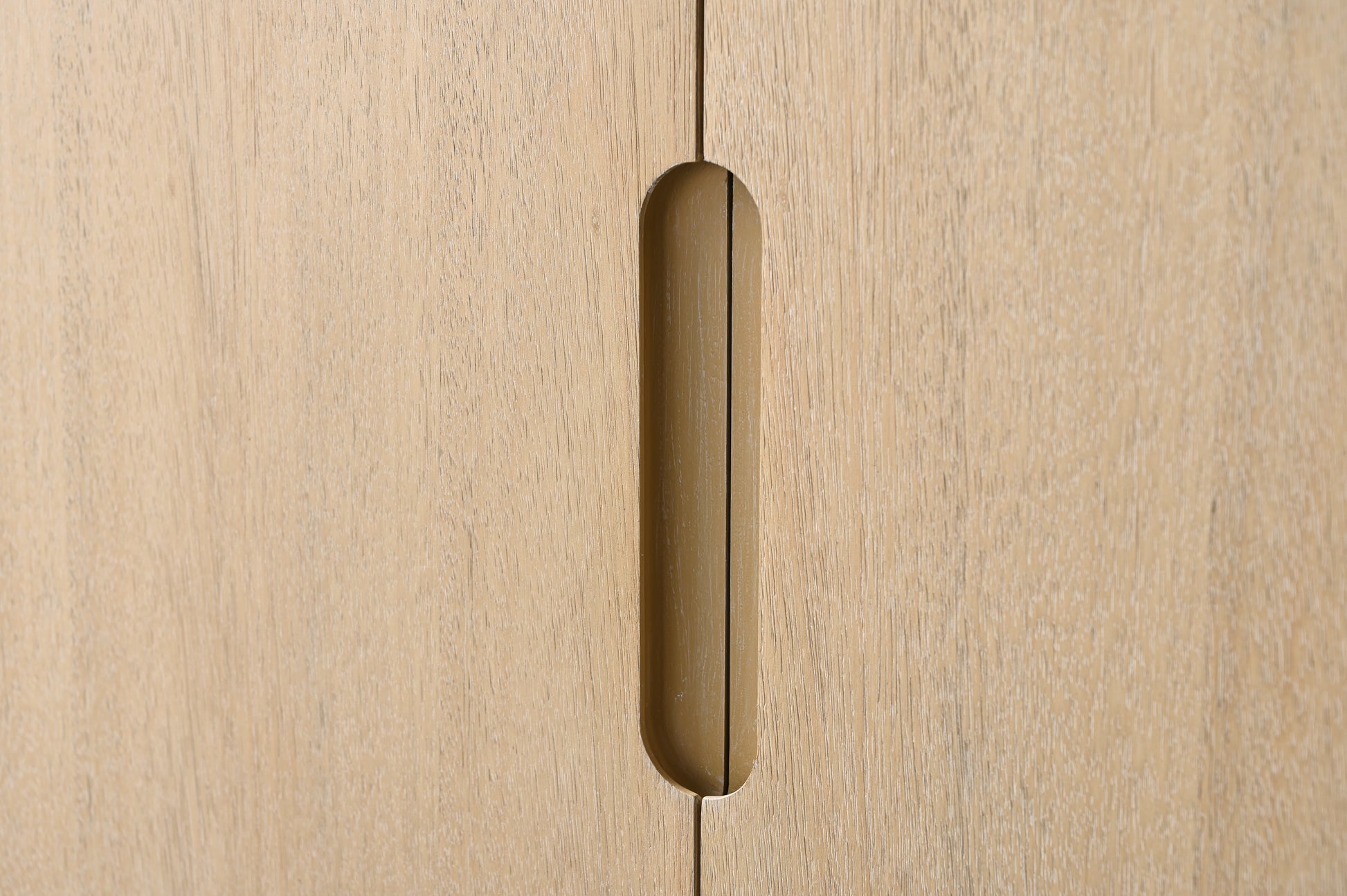 Close-up of recessed elongated brass pull handle centered on light oak double-door vanity cabinet